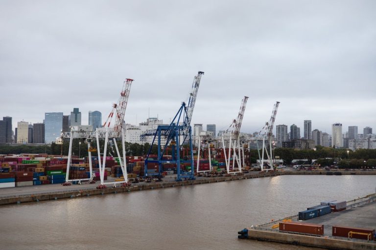 Queda de 1,7% na economia argentina eleva desafios para o governo Milei Contêineres e guindastes em um porto, com o skyline de Buenos Aires ao fundo.