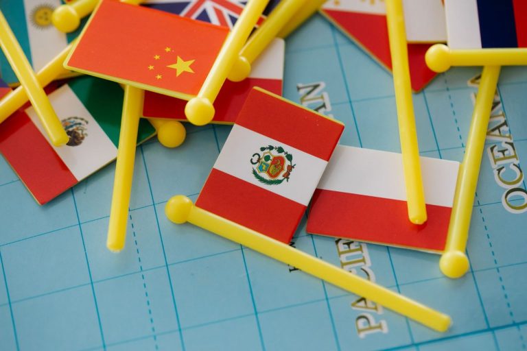 Pequenas bandeiras de diferentes países dispostas sobre um mapa-múndi, representando relações e disputas geopolíticas internacionais.